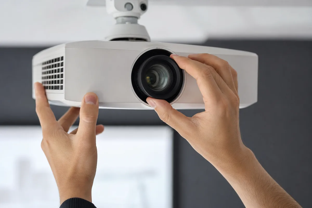 Mains ajustant la molette de mise au point d un vidéoprojecteur fixé au plafond, écran de projection en arrière-plan